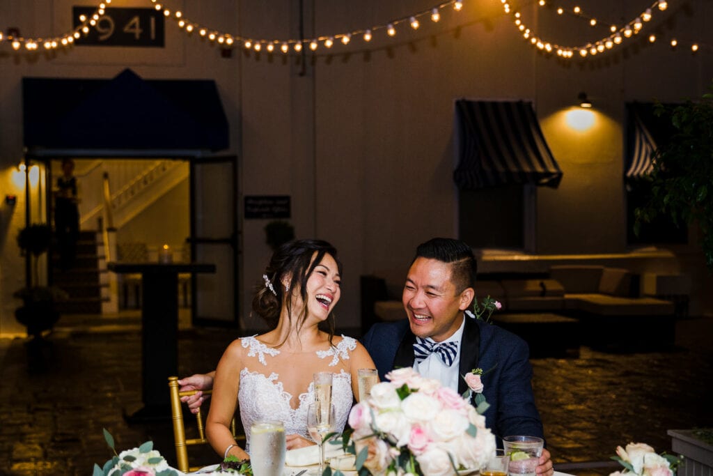 A bride and groom laughing at their sweetheart table in the tent at Regatta Place during their wedding reception