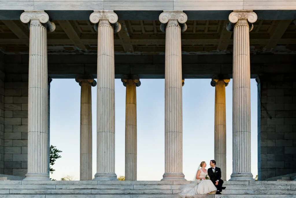 A bride and groom sitting on the steps of the temple to music at roger williams park on their wedding day