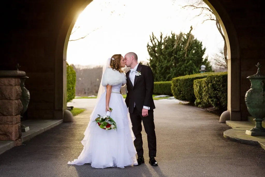 A bride and groom kissing underneath a stone archway