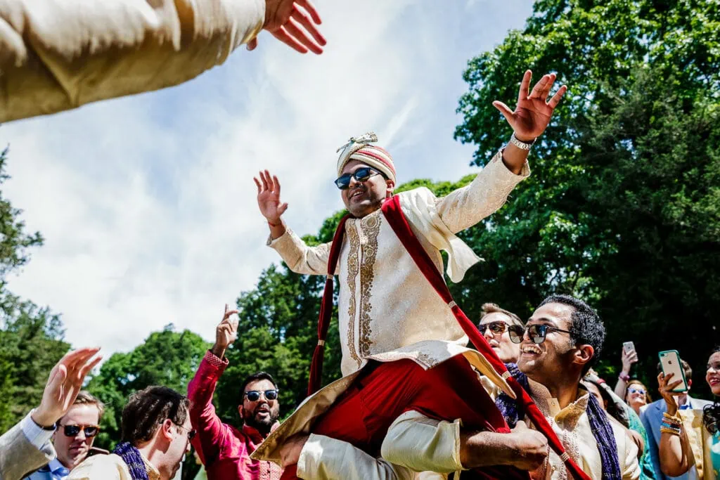 A groom in red and white indian dress is hoisted into the air at his baraat. in rhode island