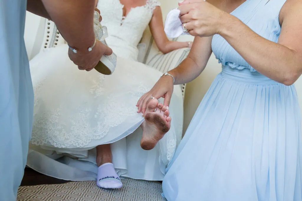 Two bridesmaids in blue help put shoes on the brides dirty feet