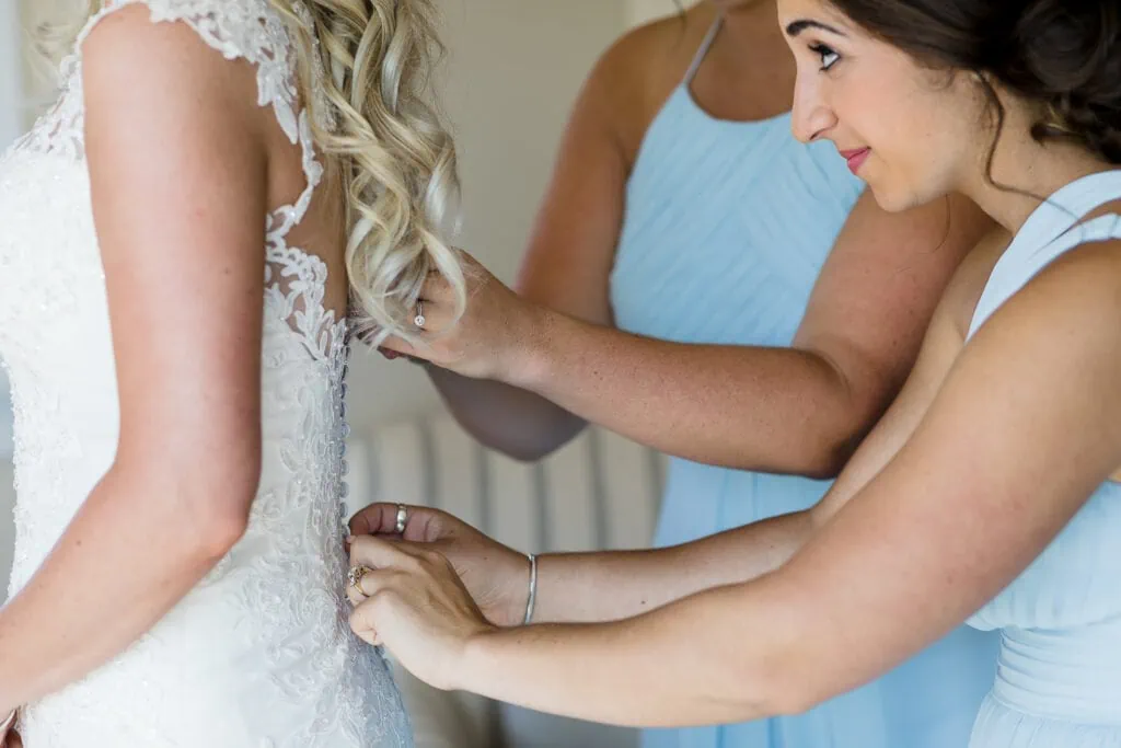 Two bridesmaids in blue help button a brides dress