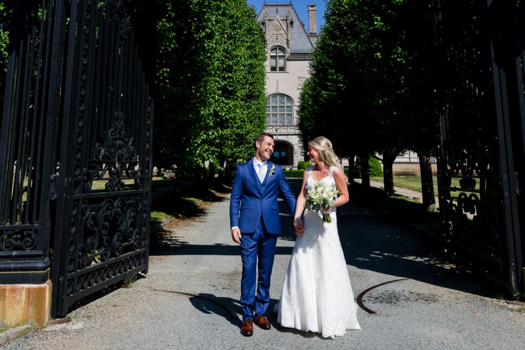 A bride and groom exiting large iron gates to a tree lined driveway and a mansion