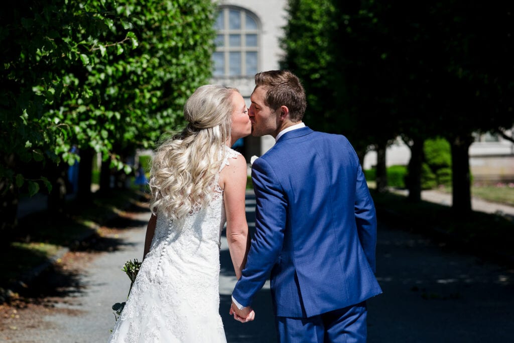 A bride and groom kissing with a tree lined driveway