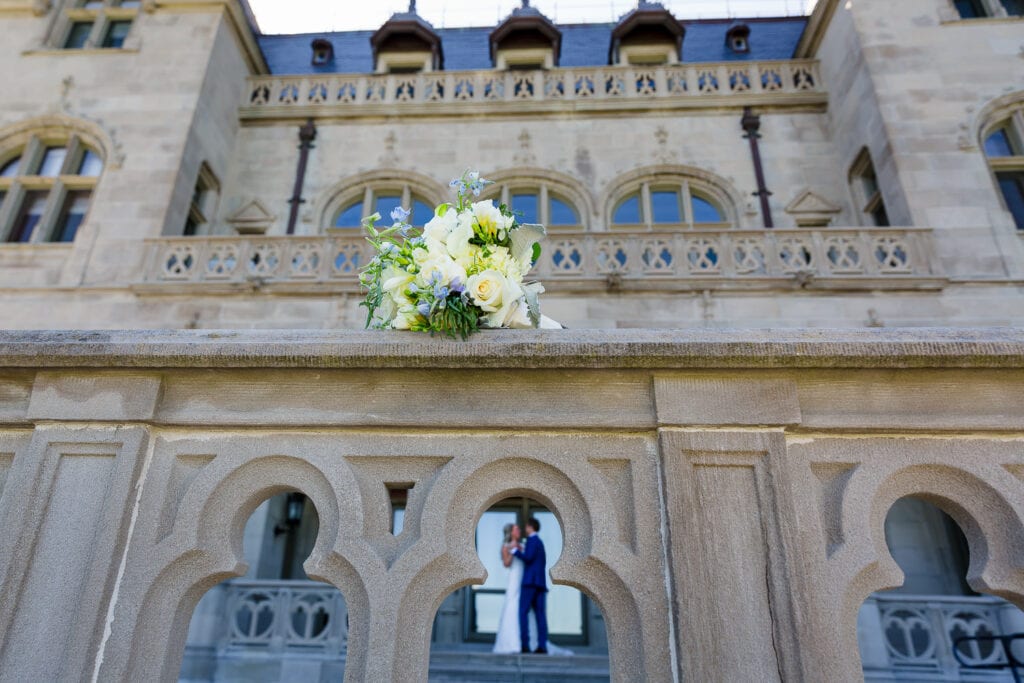 A wedding bouquet sitting on a ledge with the bride and groom in the background