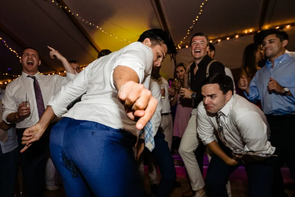 A man dances and points to the rip in his suit pants