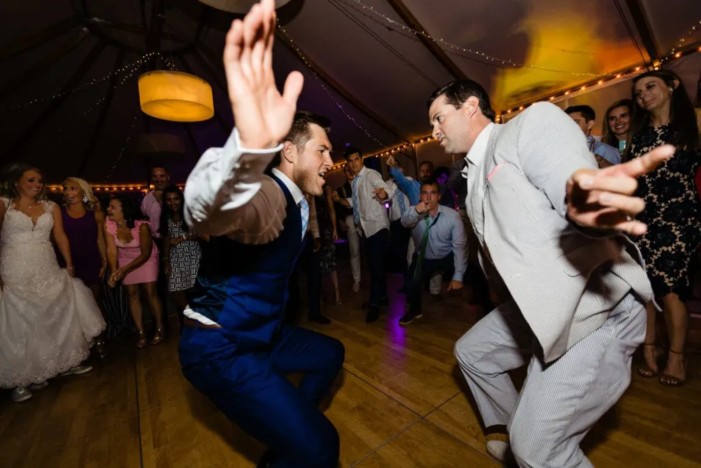 A man in blue suit dancing with his hand up with a man in a gray suit