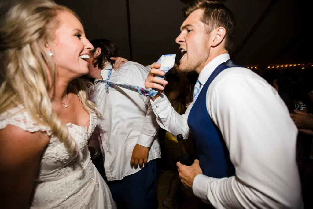 A groom holds another mans tie and sings into it like it's a microphone