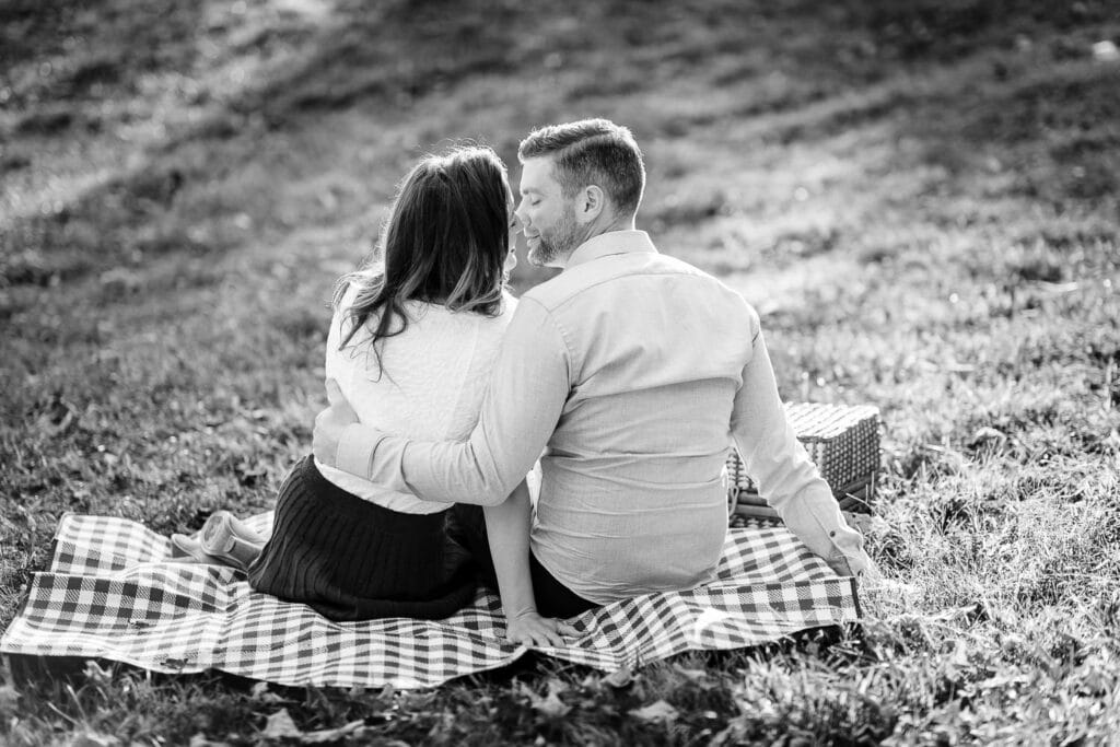 A man and woman snuggled on a gingham picnic blanket during their engagemen photography session at moore state park