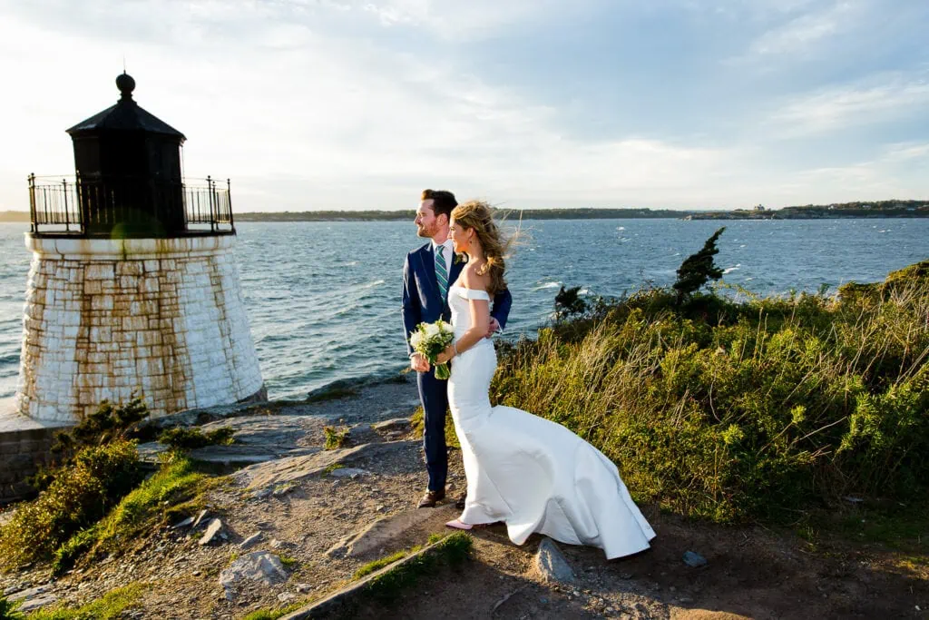 A windblown bride and groom standing by the castle hill lighthouse