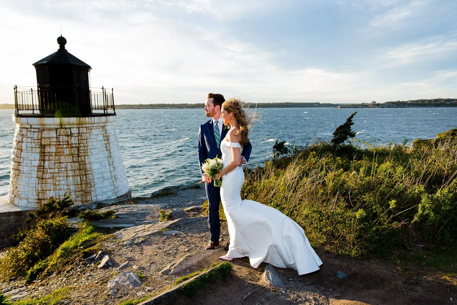 A windblown bride and groom standing by the castle hill lighthouse