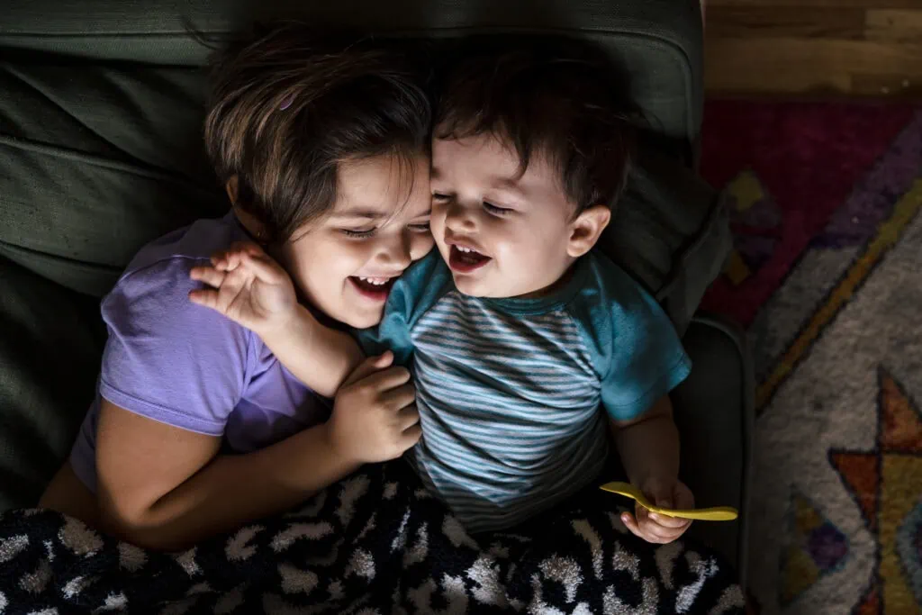 A little girl and boy siblings cuddle and laugh on the couch during a day in the life family photography session