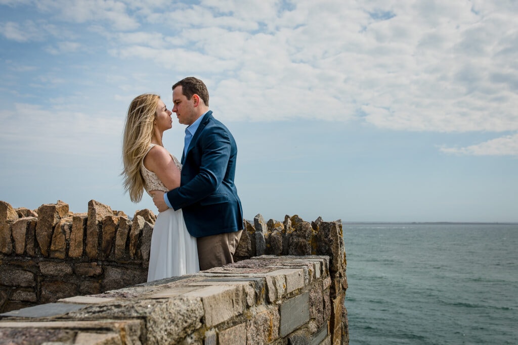 A man and woman go in for a kiss along the stone walls of cliff walk in newport ri
