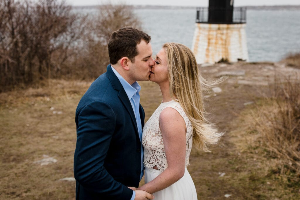 A man and woman kiss in front of the castle hill inn lighthouse during their newport ri engagement photos