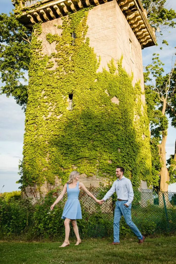 A man and woman walk by an ivy covered water tower at their harkness memorial state park engagement photo session
