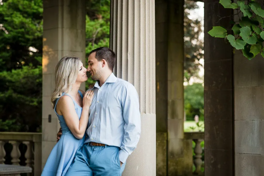 A man and woman in light blue outfits lean against a pillar in the gardens at harkness memorial state park
