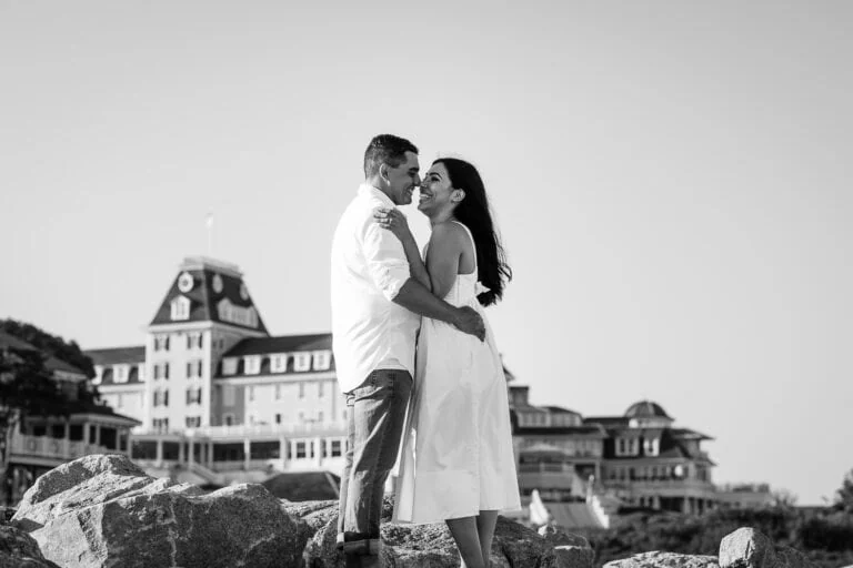 A man and woman in white embrace on rocks overlookin the ocean house hotel in watch hill rhode island