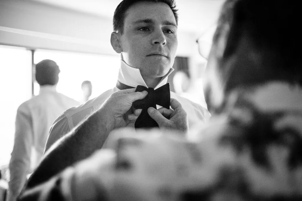 A man stairs intently as another man adjusts his bowtie