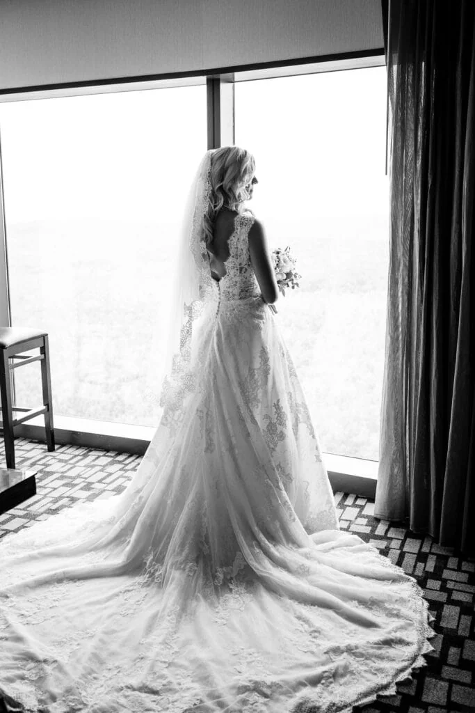 A bride with long train and veil looks out of a bright window at Fox Tower