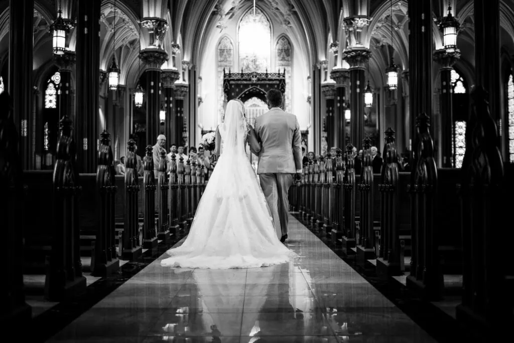 A bride and her father walking down a church aisle from the back