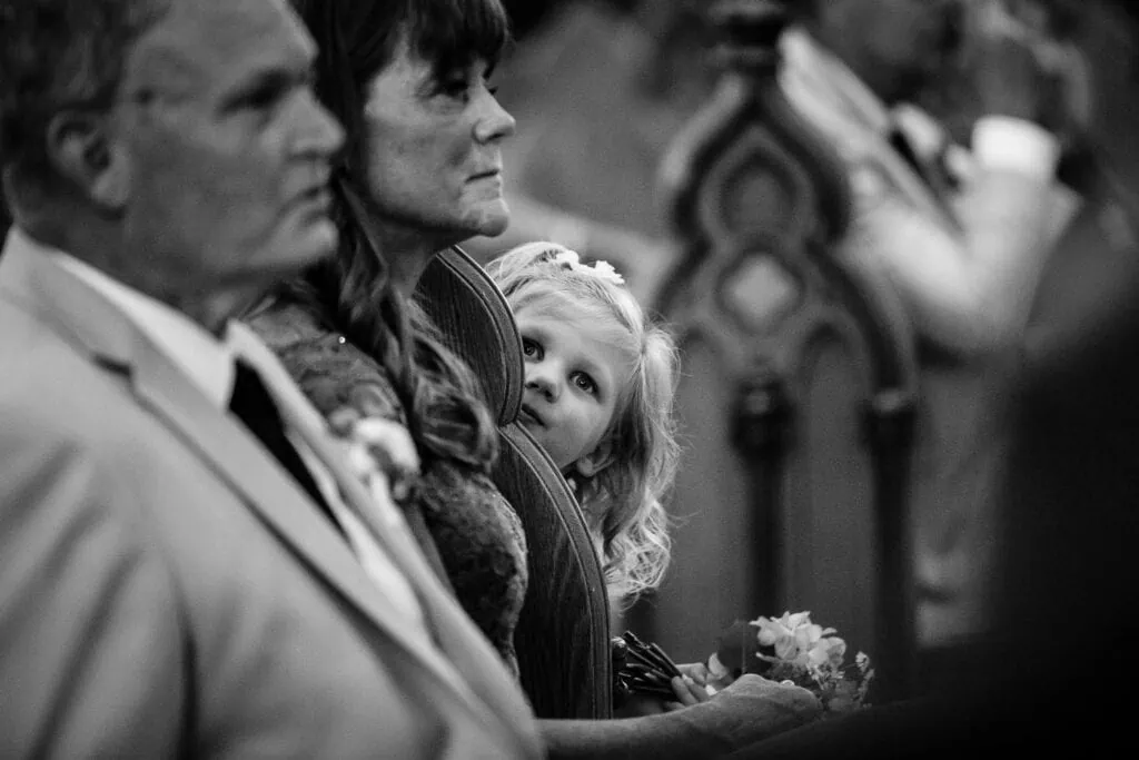 A little girl peeks out from behind a church pew