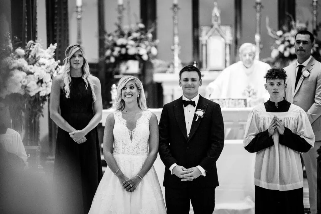 A bride laughs with widened eyes next to her groom in a church wedding ceremony