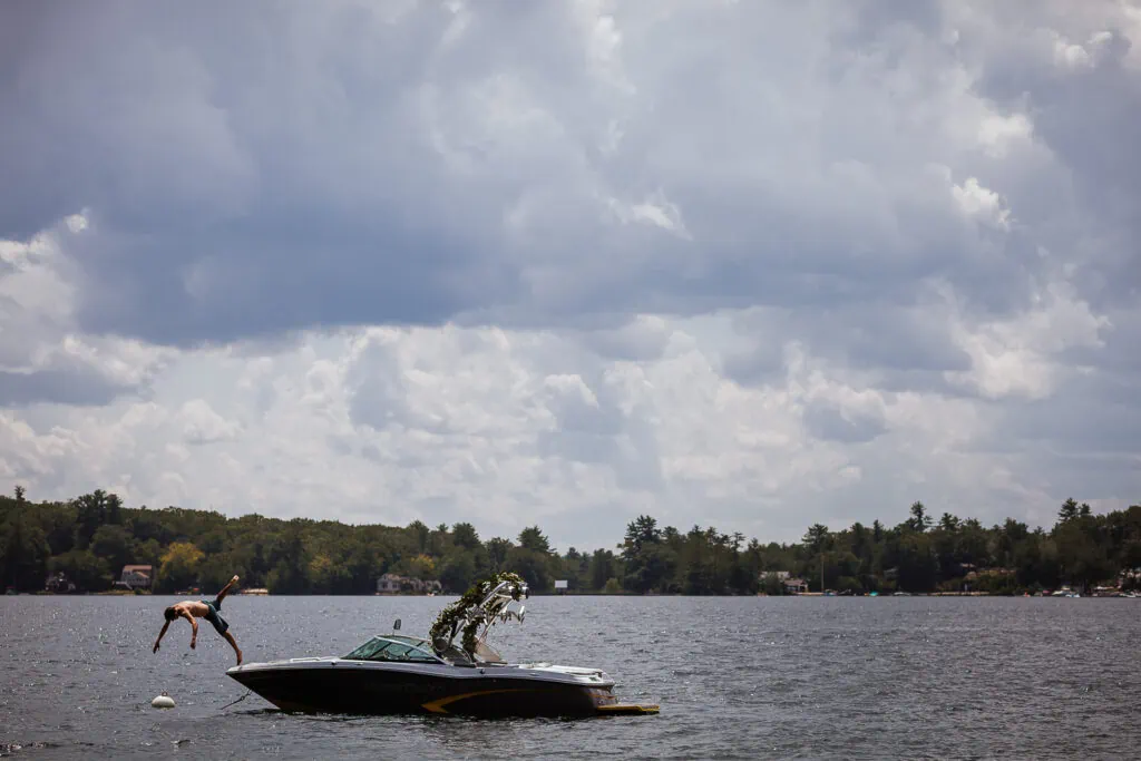 A man in a bathing suit jumps off a speedboat into a lake
