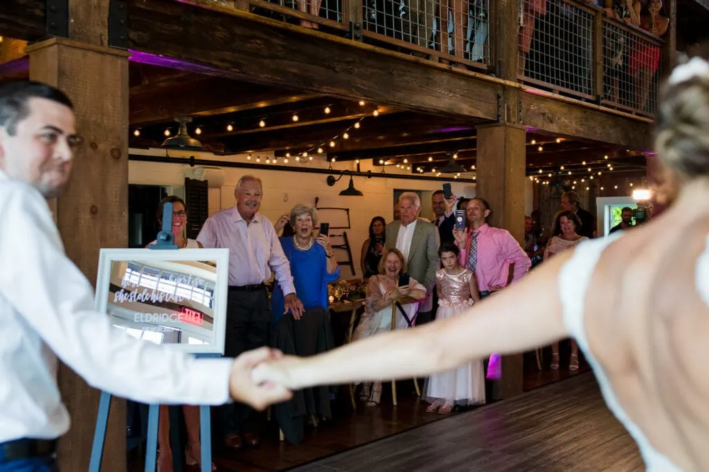 Guests in a barn react with smiles and yells as a couple makes their grand entrance