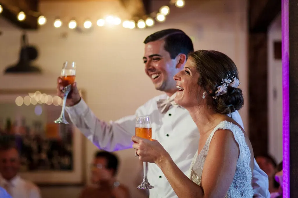 A bride and groom laugh holding champagne glasses at the Pickering House