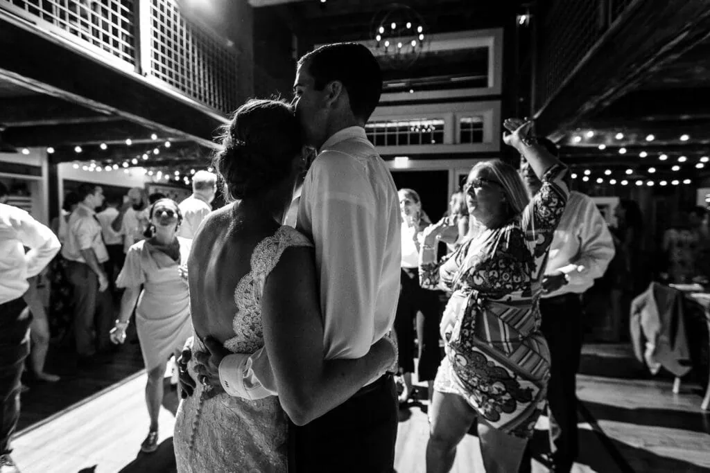 A groom embraces and kisses his brides forehead on a dance floor in a barn