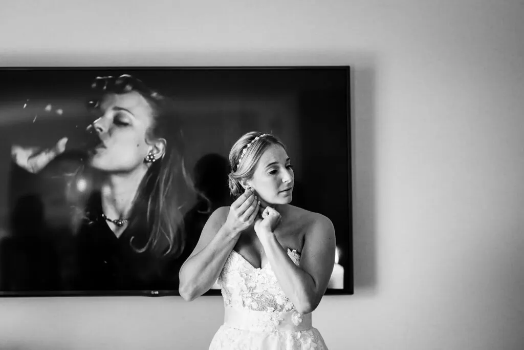 A bride adjusts her earring standing in front of a tv screen that is playing The Notebook movie