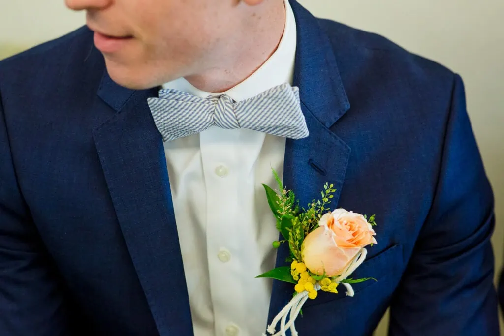 A close up of a grooms seersucker bowtie and peach rose Boutonnière