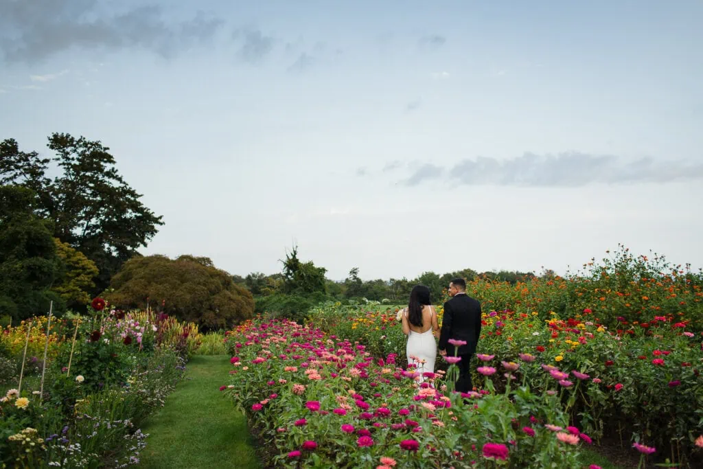 A bride and groom walking through the cut flower garden at Eolia Mansion