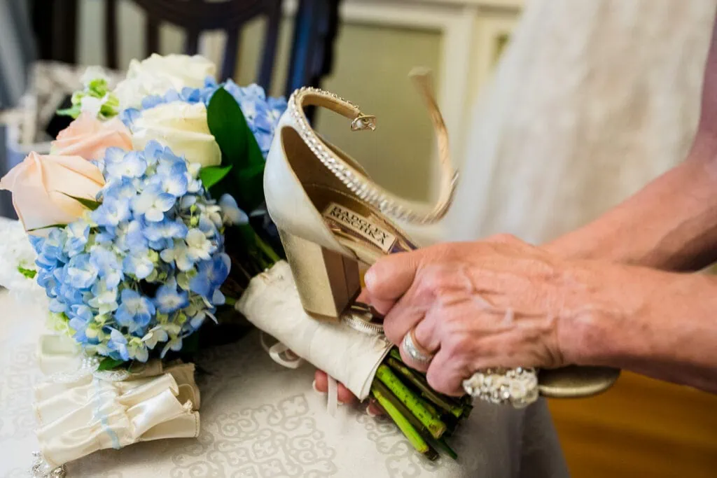 A hand holding a badgley mischka shoe uses it to hammer something into a bouquet of flowers