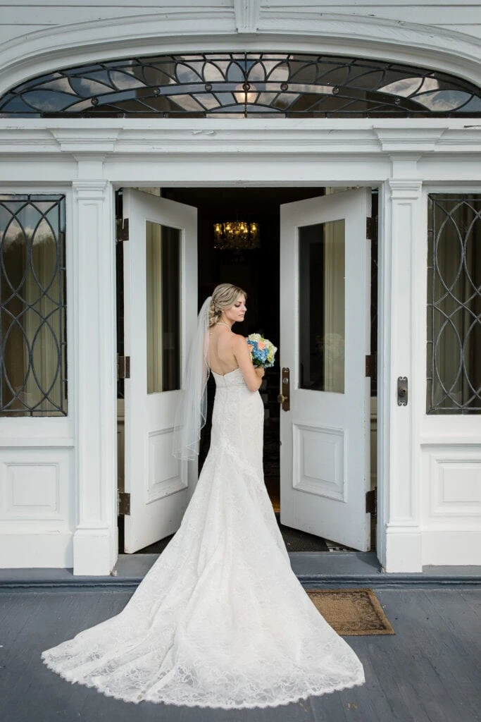 A bride in a long white train and fingerlength veil poses in the doorway of haley mansion
