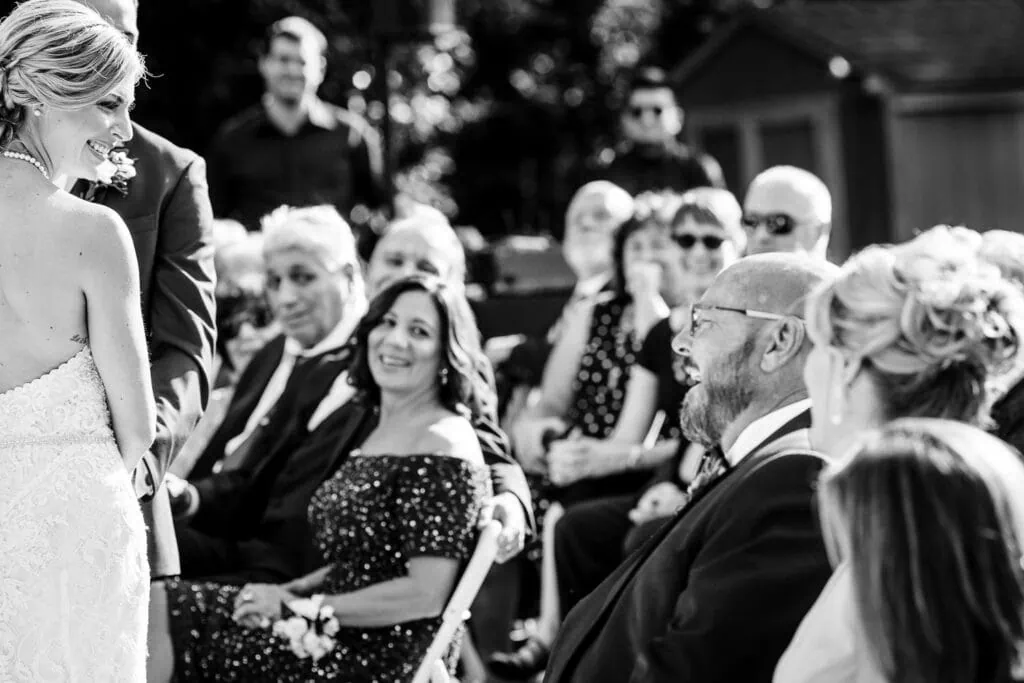 A bride and guests all look at a man in the audience of a wedding ceremony