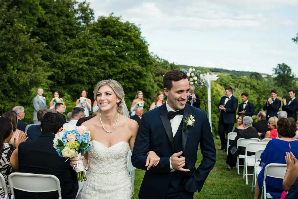 A groom sticks out his tongue and give the hang ten hand signal as he walks arm and arm with his bride out of the wedding ceremony outdoors