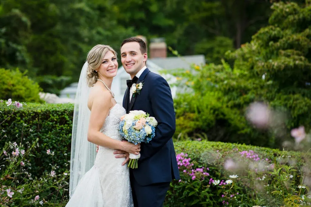 A bride and groom smiling for a wedding portrait in the gardens at the Inn at Mystic
