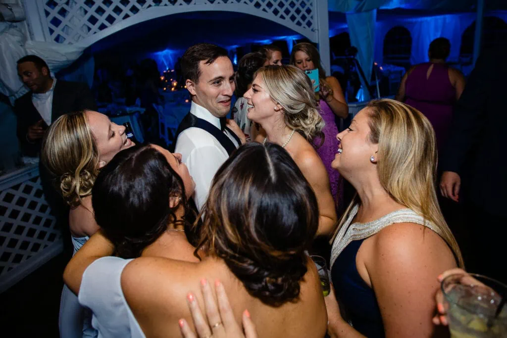A groom has a horrified look on his face surrounded by singing bridemaids