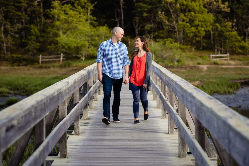 An engaged couple hold hands and walk down uncle tim's bridge in wellfleet