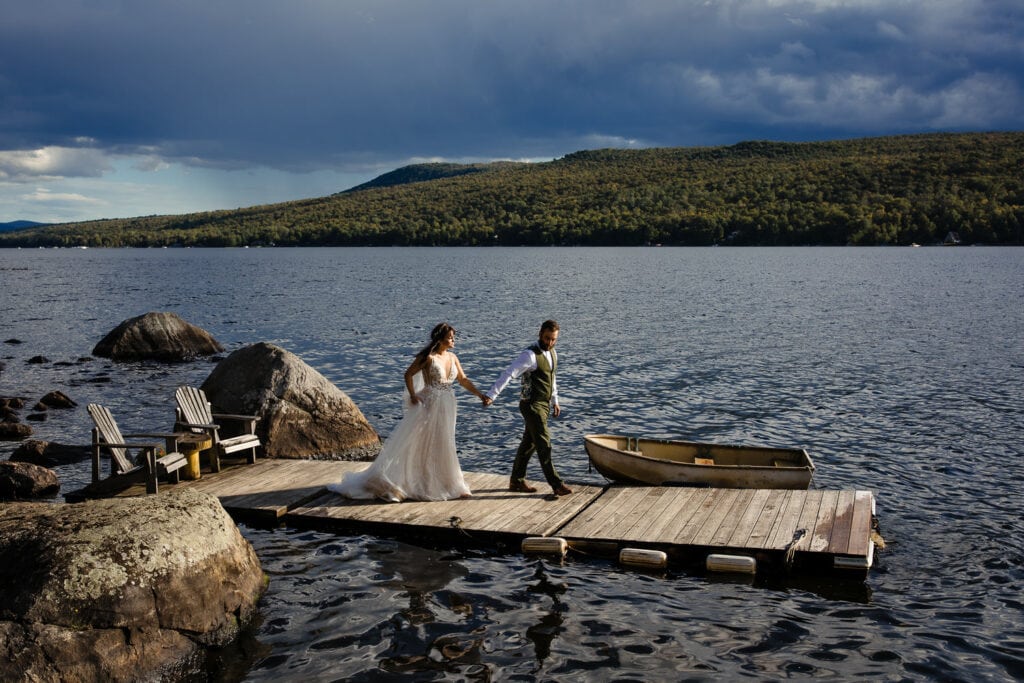 A bride and groom walk a dock hand in hand at an adirondacks lake wedding