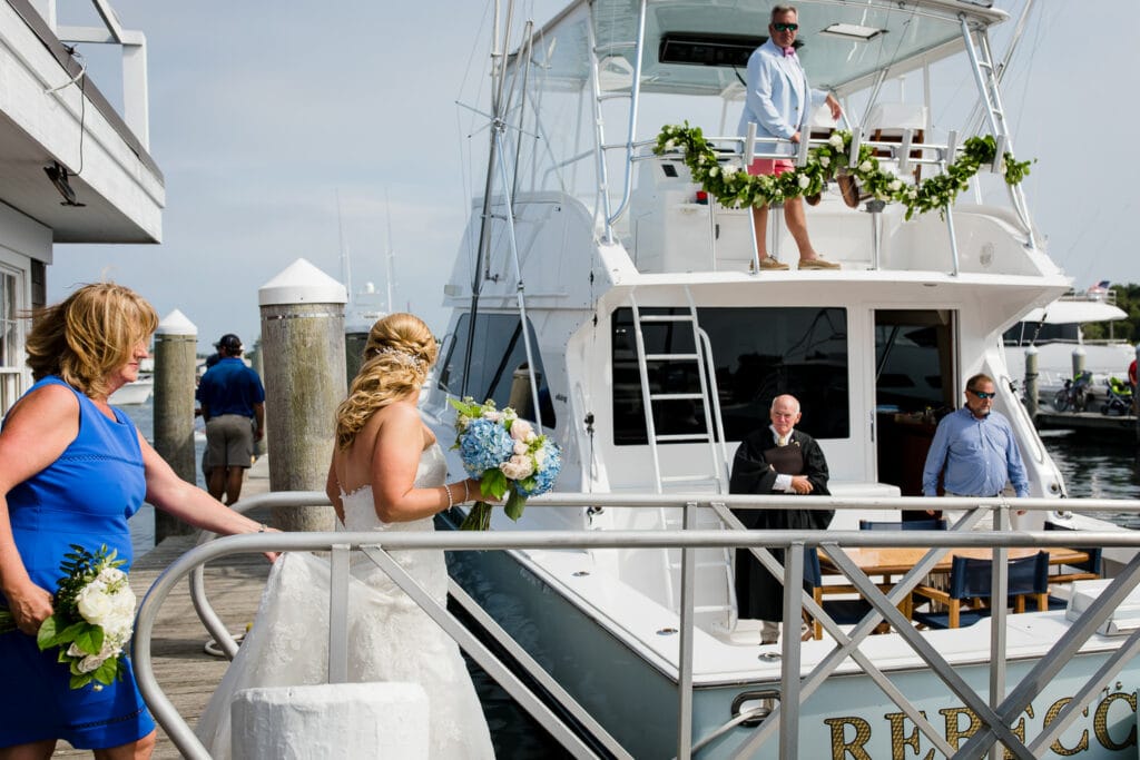 A bride walks onto a boat for her block island wedding as the officiant and groom look on from the boat