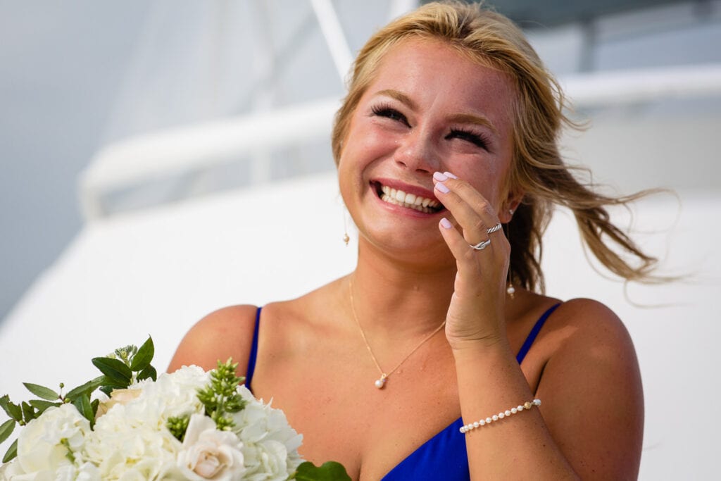 A bridesmaid smiles as she dabs a tear away from her eye