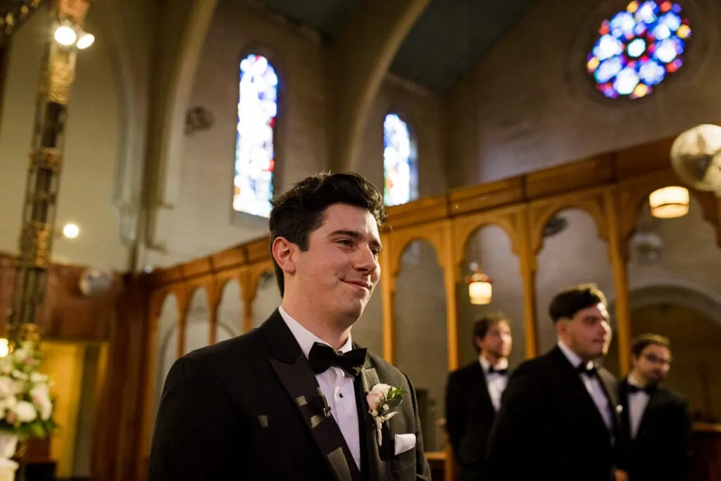 A groom smiles standing at the alter of a church