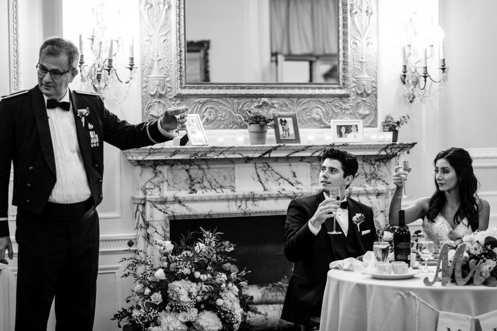 A father in military dress raises a glass to toast his daughter and new son in law sitting beside him