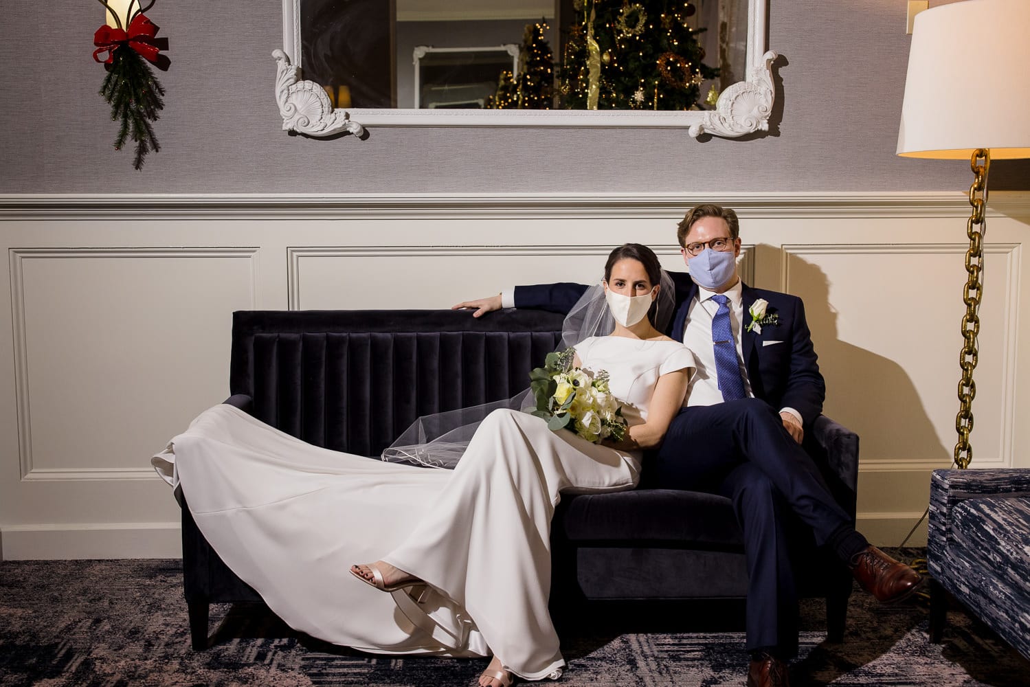 A 2020 bride and groom pose for wedding photos on a velvet couch wearing face masks