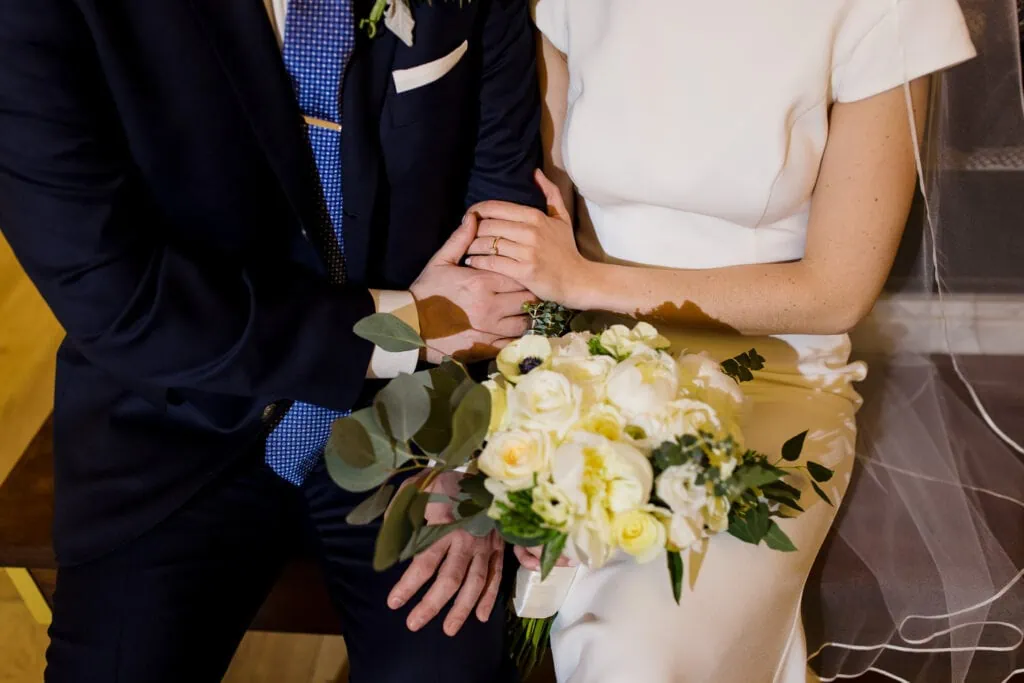 A woman in white holding flowers and man in a navy suits arms are holding each other