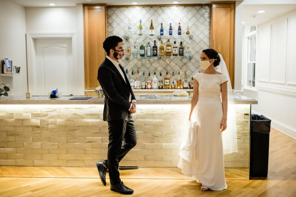 A bride and her brother chat at the bar wearing face masks.