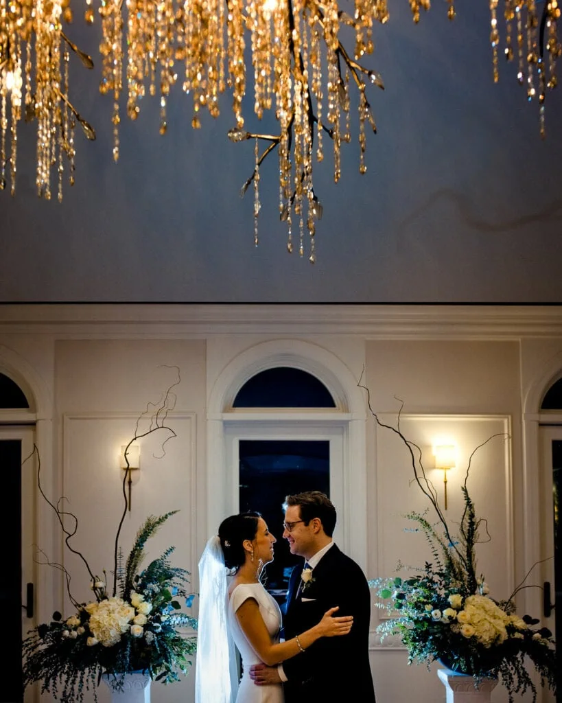 A bride and groom look at each other beneath a chandelier