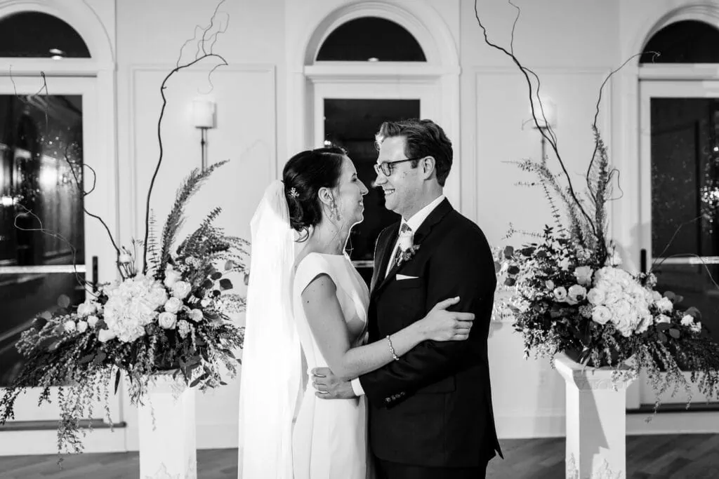 A bride and groom look at each other inbetween floral arrangements
